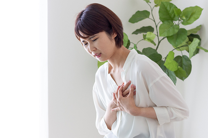 胸に痛みを感じ手を当てる女性